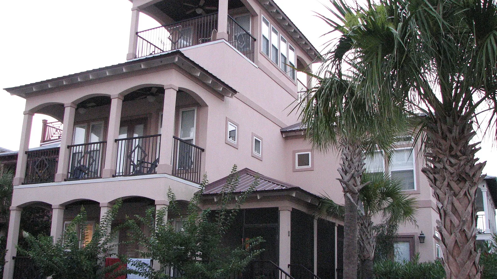 Pink stucco Rosemary Beach house with arched loggias, iron balconies, a rooftop tower and palm trees