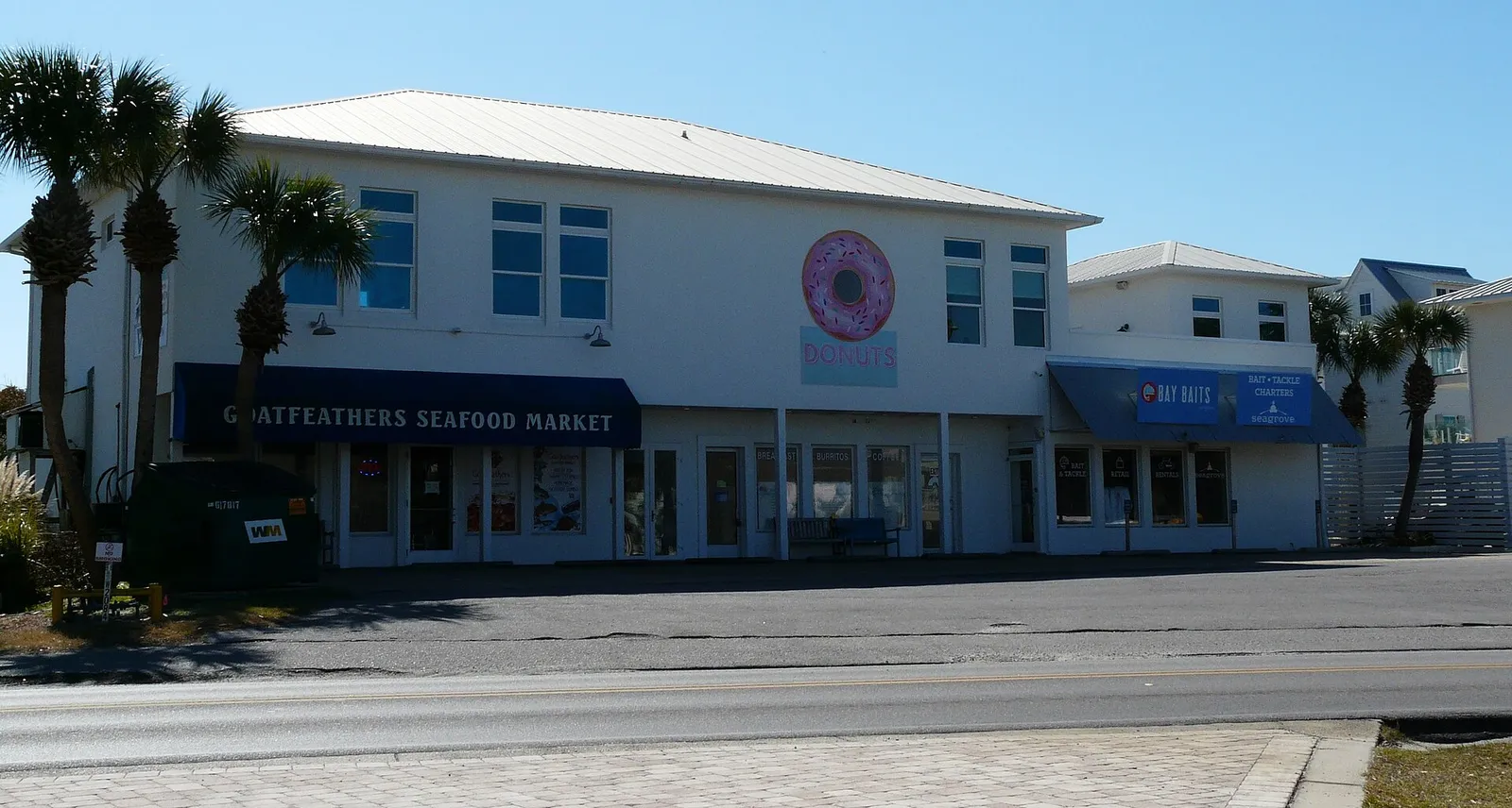 White building housing Goatfeathers Seafood Market beside County Road 30A in Seagrove Beach, with palm trees out front