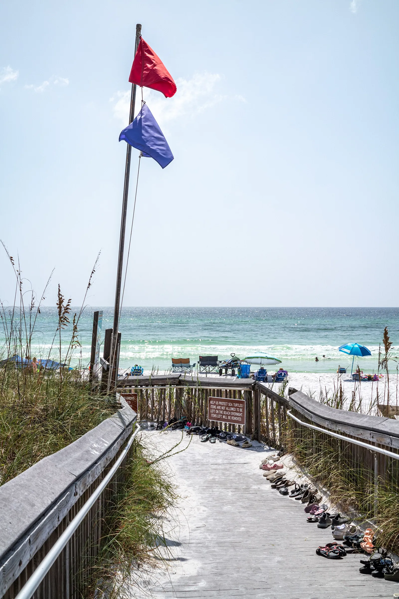 Red and purple beach warning flags on a pole above a wooden walkover leading to the beach at Topsail Hill Preserve State Park