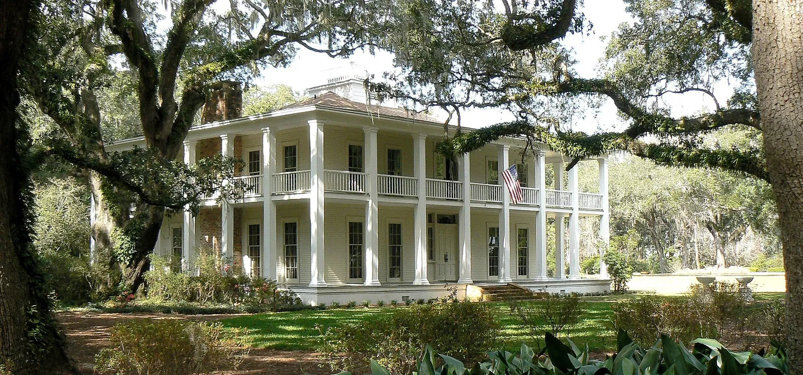 Two-story white-columned Wesley House with wraparound porches under spreading live oaks at Eden Gardens State Park