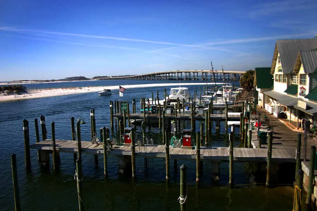 Wooden docks and boat slips on Destin Harbor with a long bridge and blue sky in the distance