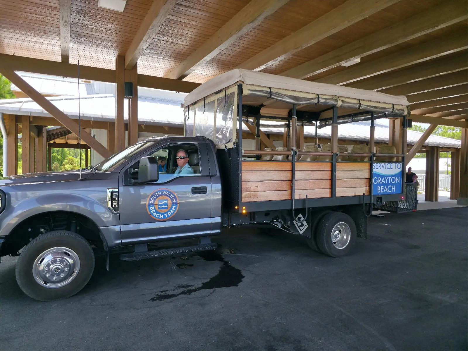 Open-air beach tram pulled by a pickup truck under the covered pavilion at the Grayton Beach Park and Ride